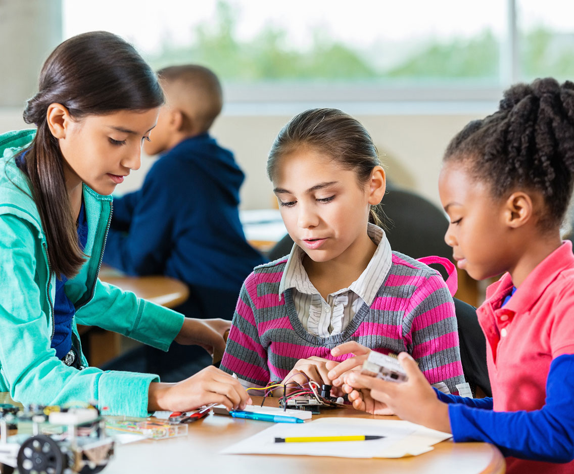 Three young girls work together on a project in a classroom