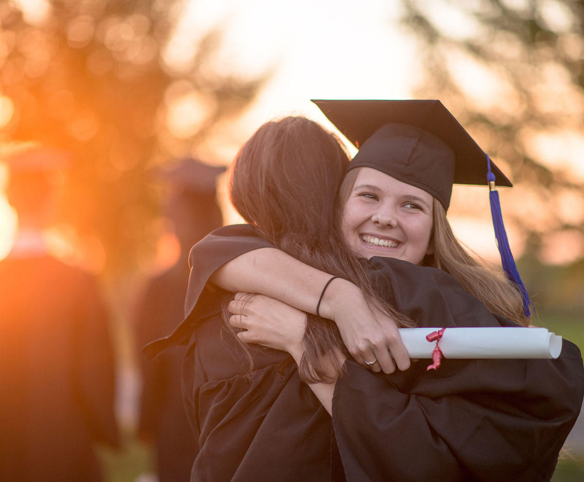 A high-school graduate hugs a family member at graduation